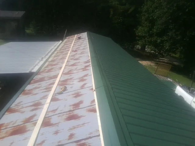Old rusted panels beside newly installed green metal roofing — Wind Damage Roof Repair by Roofing Brothers in Ackworth