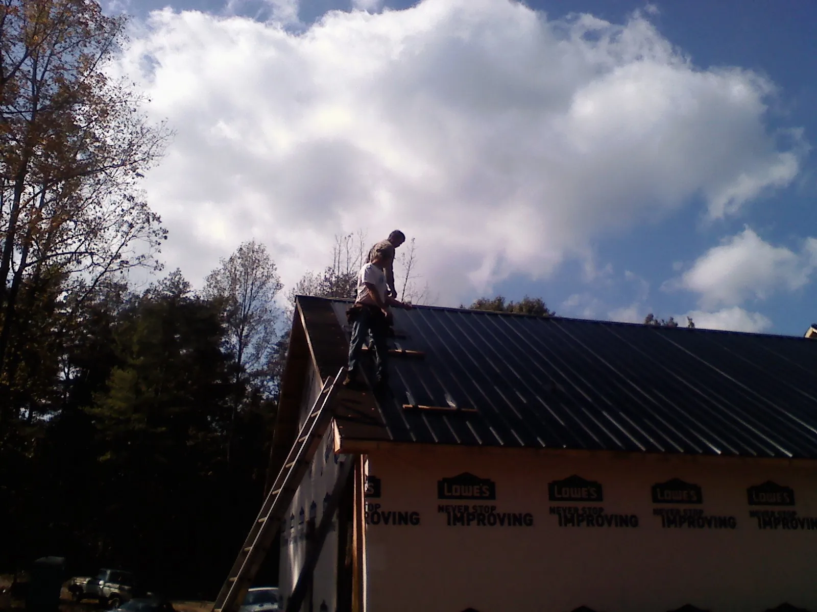 Roofer fastening dark metal panels high against a cloudy sky, from a Roof Inspection job in Ackworth