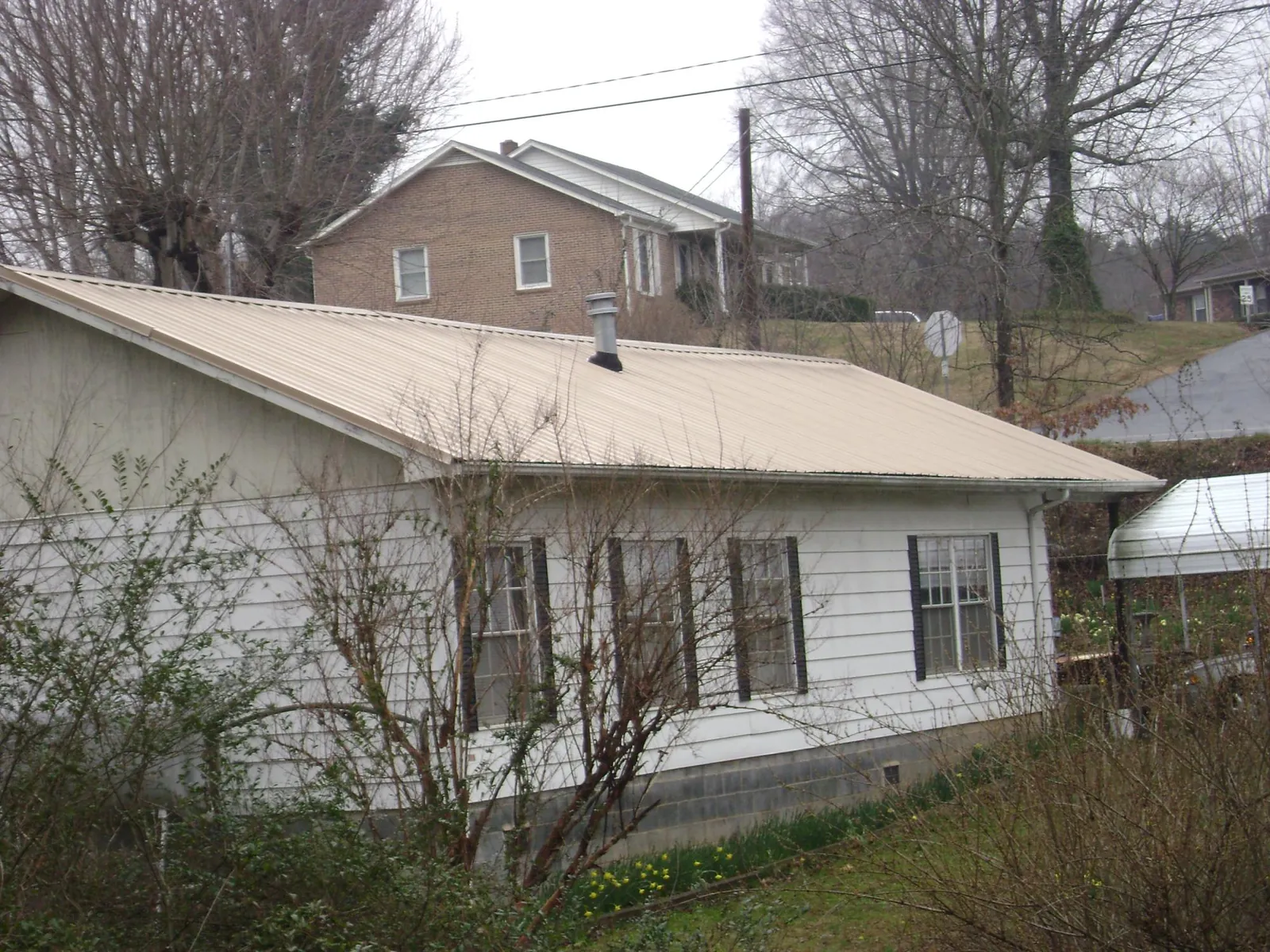 Tan metal roof on a white sided house set into a hillside — Commercial Roofing by Roofing Brothers in Ackworth
